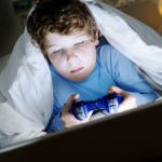 un enfant se planque sous ses draps pour jouer a la console