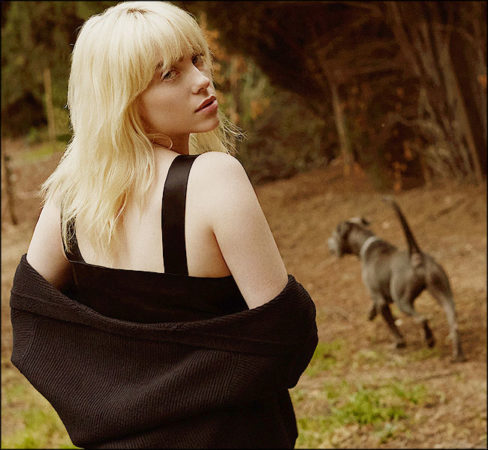 Femme blonde promène son chien en se retournant vers nous