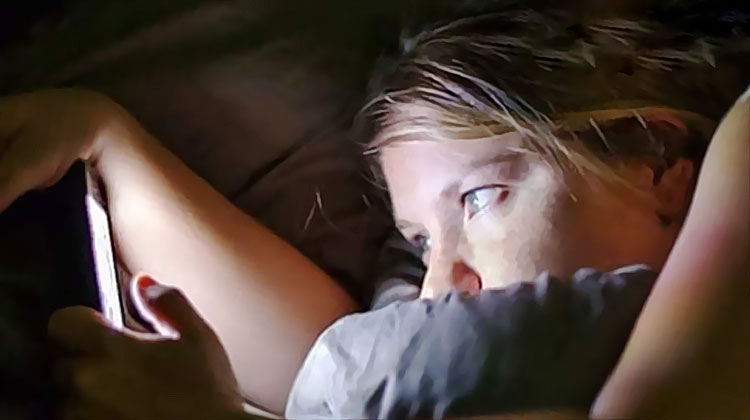 une jeune femme utilise en cachette son telephone dans son lit