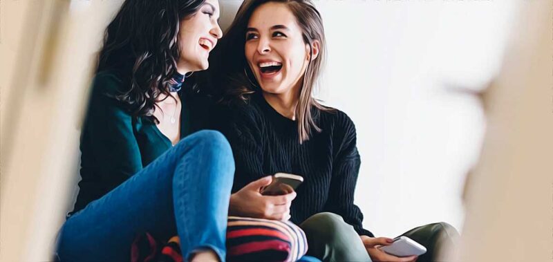 deux jeunes femmes rient aux eclats avec leur telephone en main