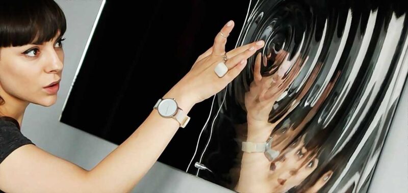 Femme touchant une surface réfléchissante ondulée.