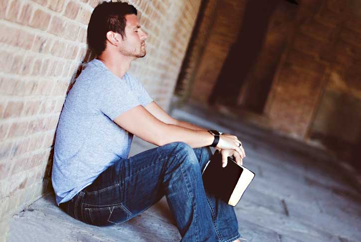 Homme assis tenant un livre couloir en brique.