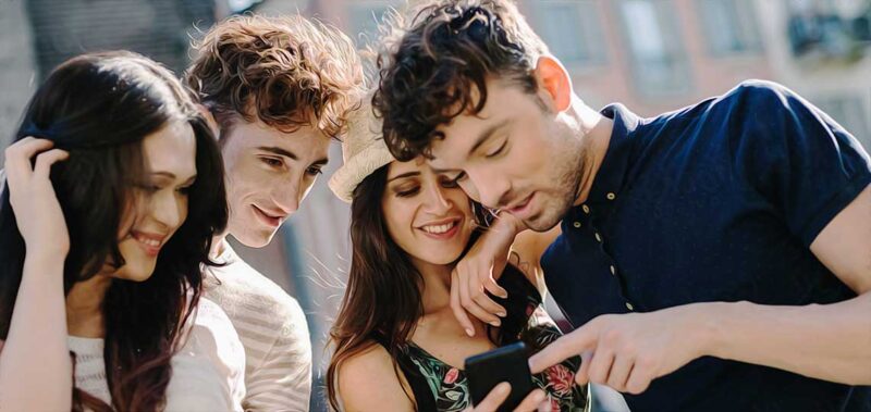 Quatre amis regardant un smartphone ensemble.