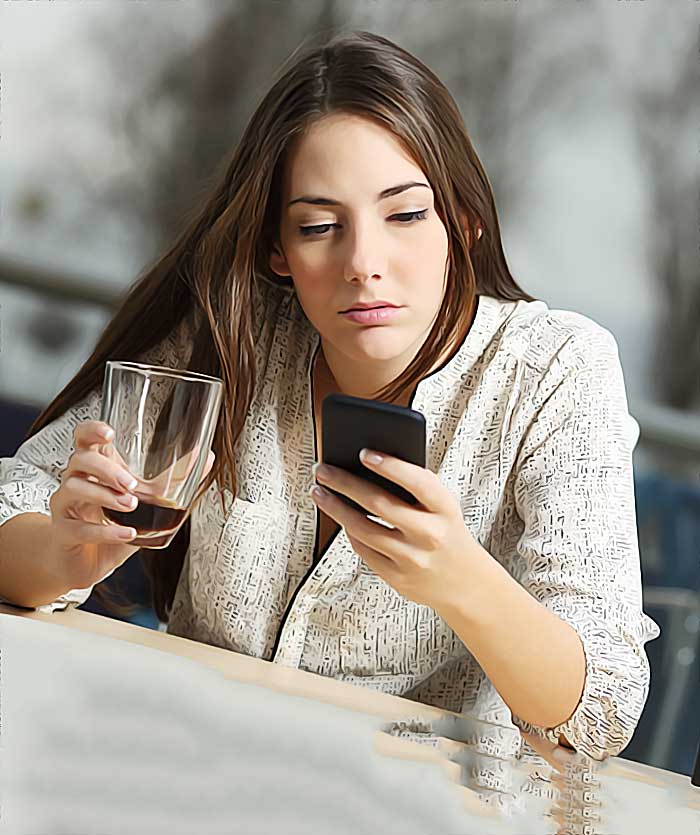 Femme consultant son smartphone en buvant un verre.