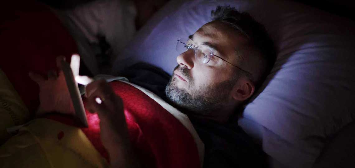 Homme utilisant smartphone dans le lit la nuit.